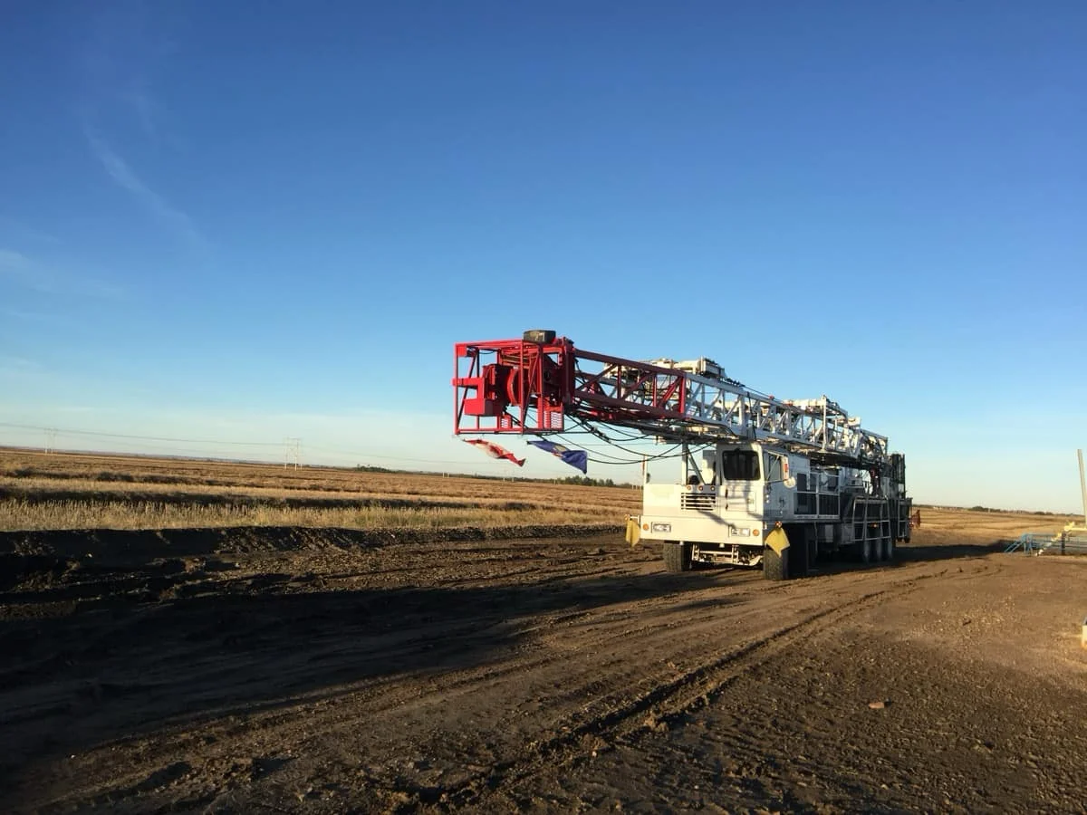 A mobile service rig laid over on a clear blue sky, parked on a lease road, ready to move to the next job site.